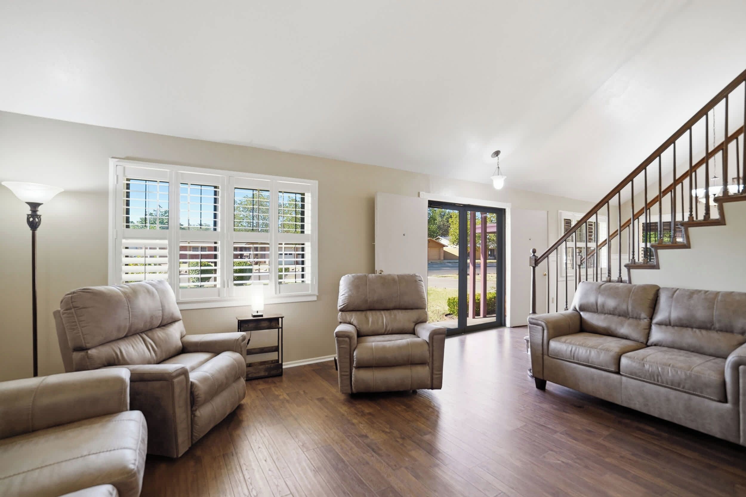 A spacious living room with a wooden floor, two leather sofas, a small table, and a staircase leading to another level.