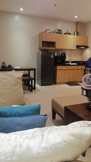 Ein Wohnzimmer mit einer Couch, einem Couchtisch und einem Esstisch. Es gibt eine Küchenzeile mit Schränken, einem Kühlschrank und einer Mikrowelle.