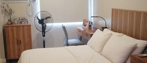A bedroom with a bed, bedside tables, a wooden cabinet, a standing fan, and an air conditioning unit.