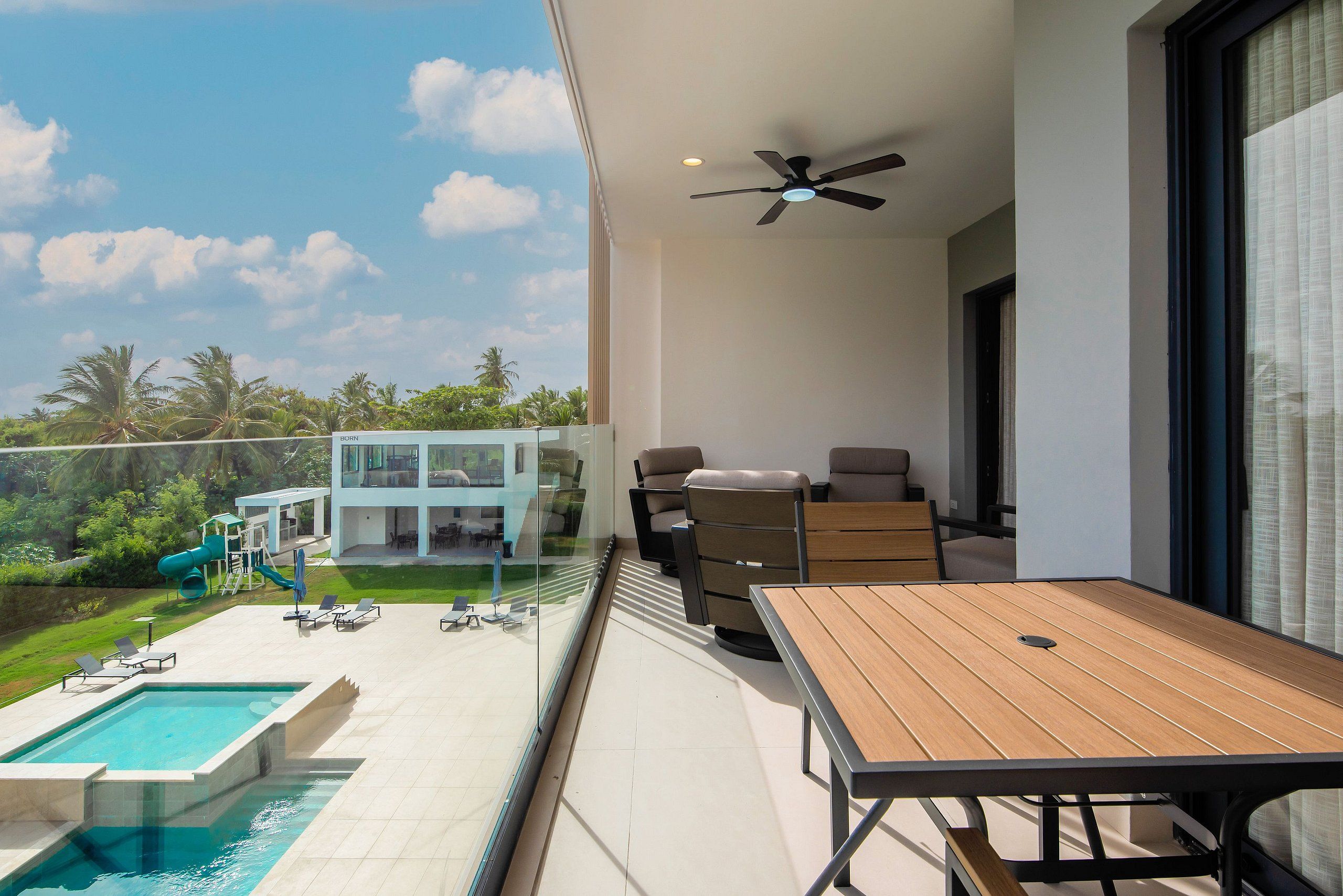 Un balcón con piscina, mobiliario exterior y vistas a un edificio moderno con fachada de vidrio.