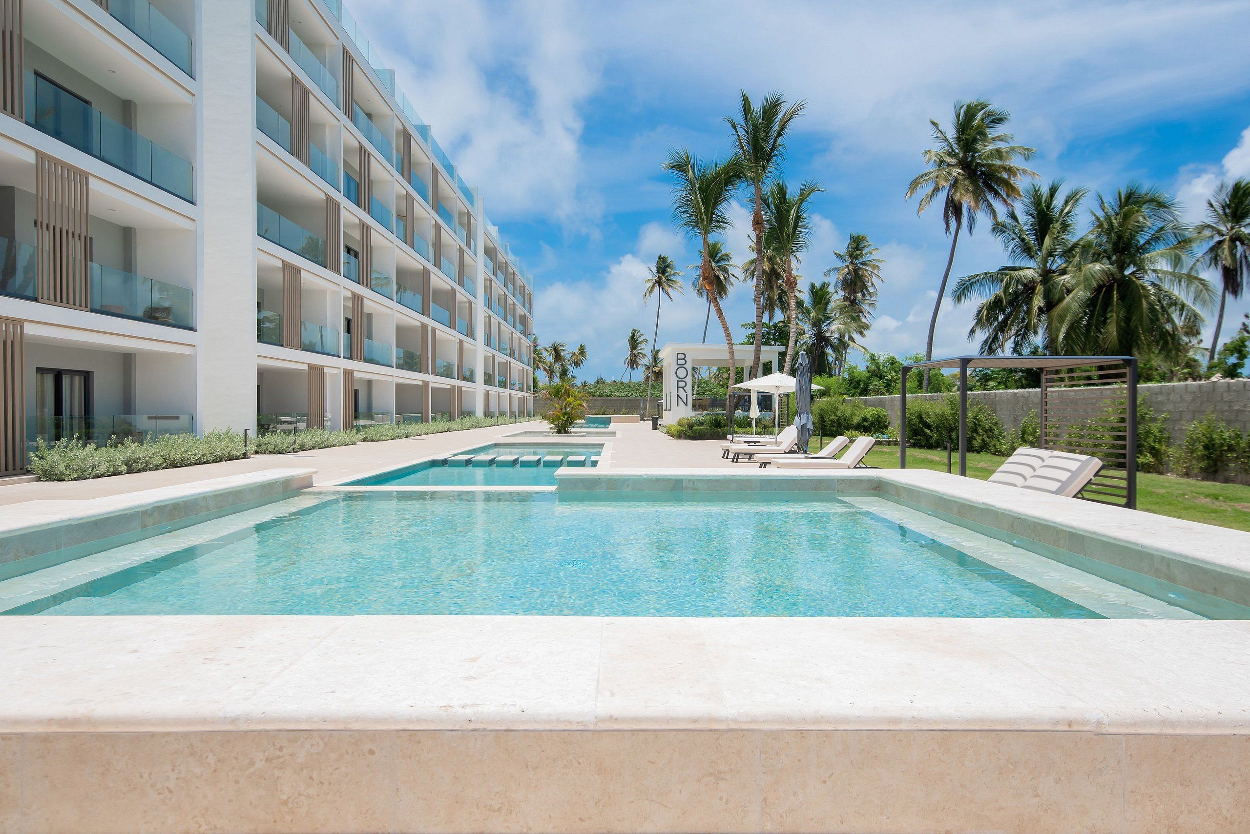 Ein modernes Hotel mit Swimmingpool, Palmen und blauem Himmel.