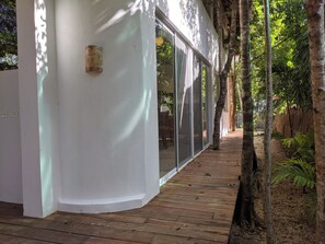 A wooden deck leading to a modern building with large glass doors, surrounded by trees. - Casa Natik - A Mayan House in the Jungle. Ideal for families and ecotourism (Chemuyil (jungle))