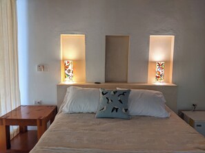 Un dormitorio con una cama, almohadas, una mesita de noche y dos lámparas de pared.