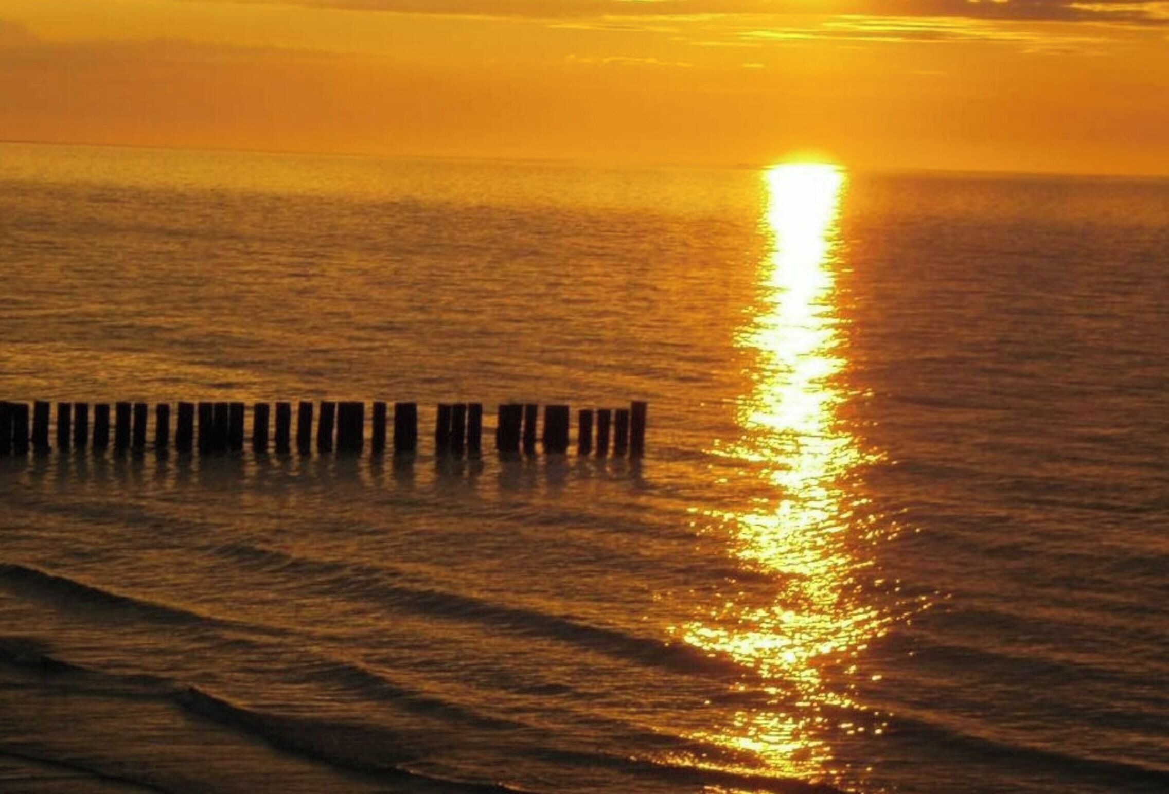 A sunset over a calm sea with wooden posts in the foreground.