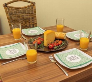 Un desayuno con un plato de queso y tomates, dos vasos de zumo de naranja y una cesta al fondo.