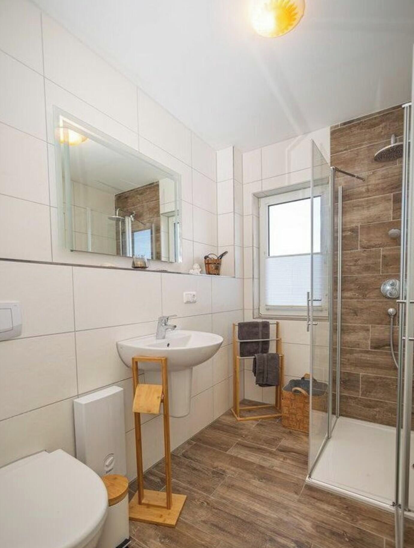 A modern bathroom with a white sink, mirror, and a glass-enclosed shower.