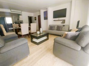 A modern living room with a sofa, armchairs, a coffee table, and a flat-screen TV mounted on the wall. - Acapulco Diamante / Jacuzzi / Club de Playa (Acapulco de Juárez)