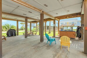 Eine offene Terrasse mit Picknicktischen und -stühlen, einem Grill und Blick auf eine Wohngegend.