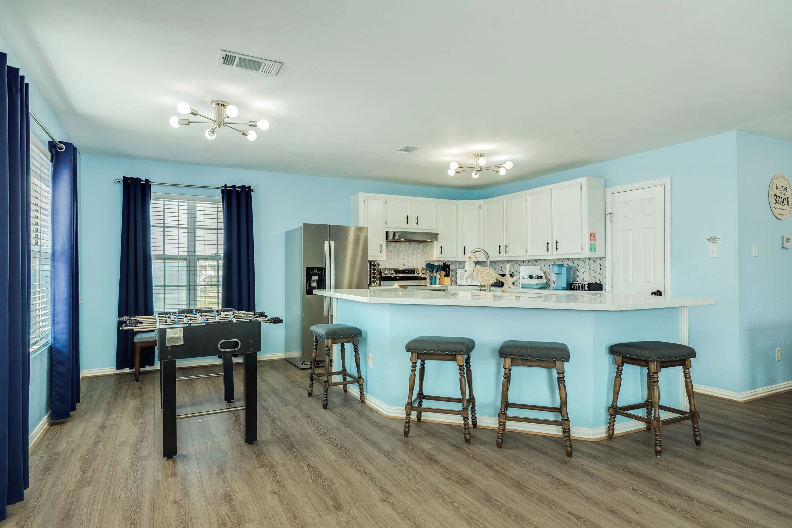 A modern kitchen with white cabinets, a central island with stools, and a foosball table.