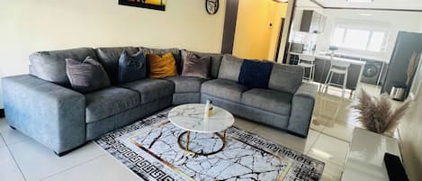 Una sala moderna con un sofá seccional gris, una mesa de centro de mármol y una alfombra estampada.