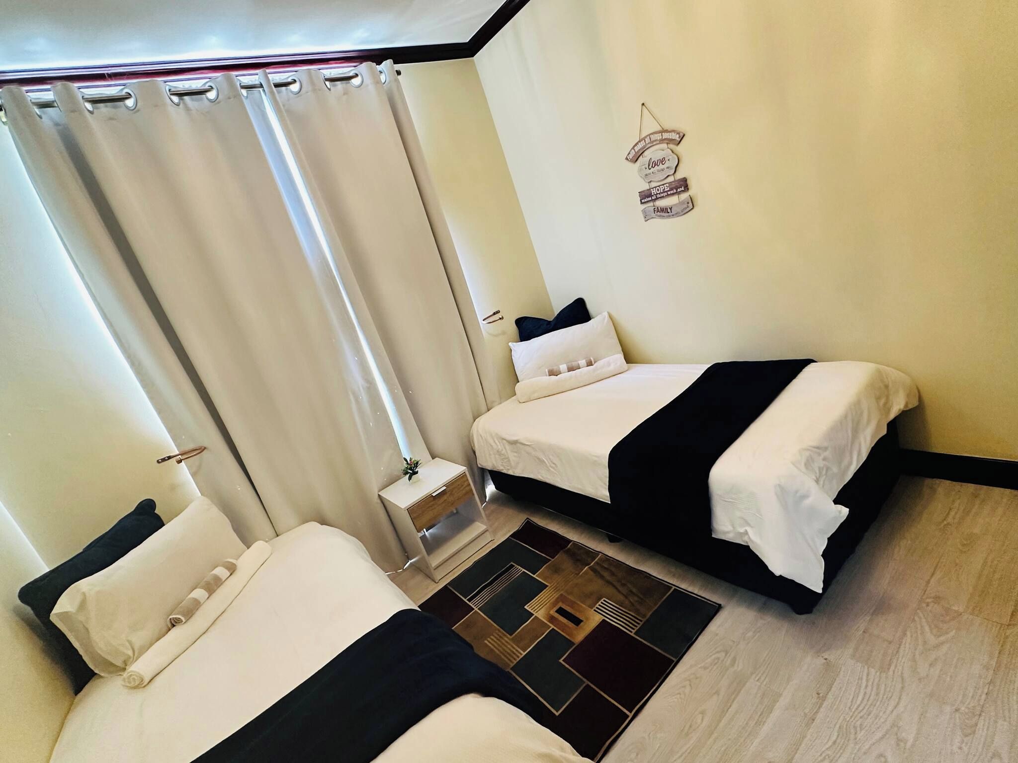 A hotel room with two beds, a small bedside table, a nightstand, a decorative wall sign, and a patterned rug.