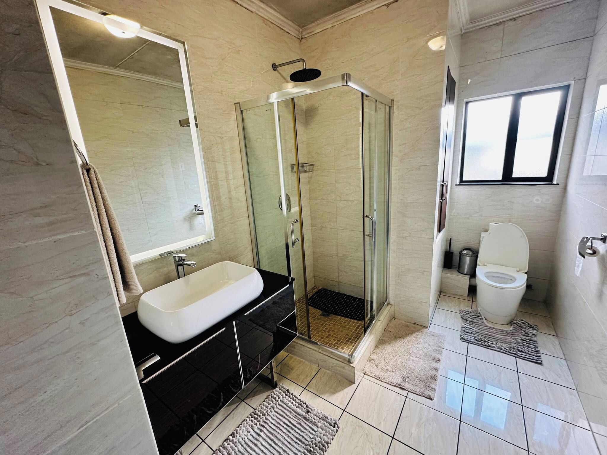 Ein modernes Badezimmer mit einer in Glas abgeschirmten Dusche, einem weißen Waschbecken und einer Toilette.