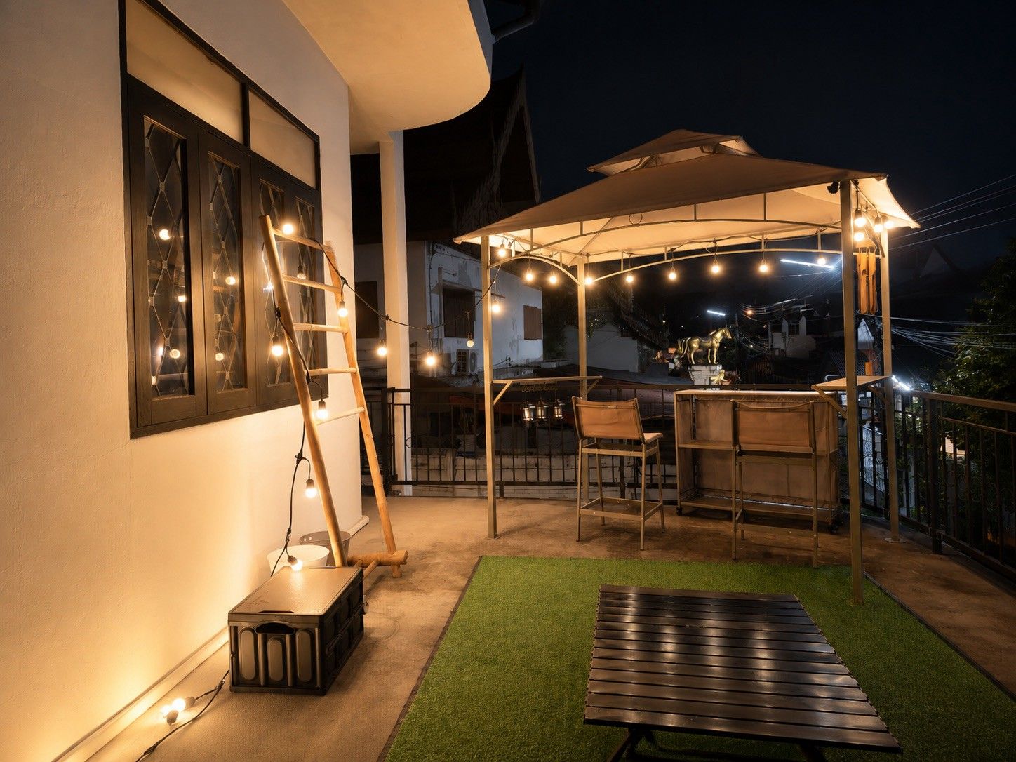 An outdoor patio area with a covered seating area, a wooden bench, and a ladder leaning against a wall.