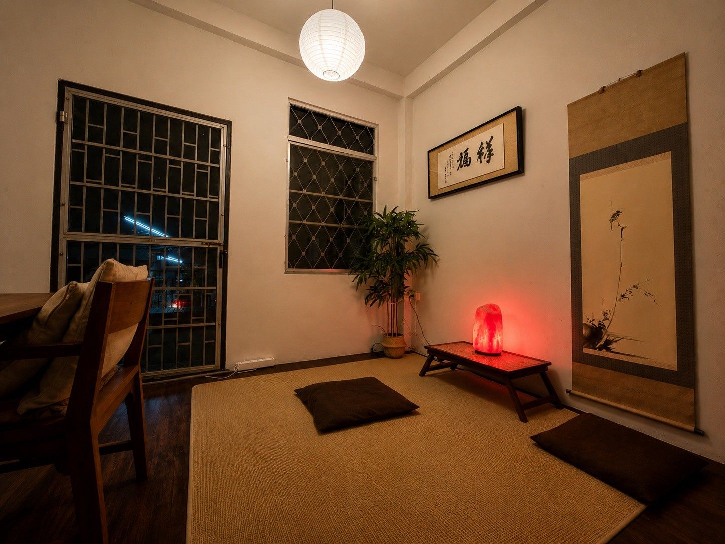 Quarto com cama, uma cadeira, planta em vaso, luz vermelha e obras de arte na parede.