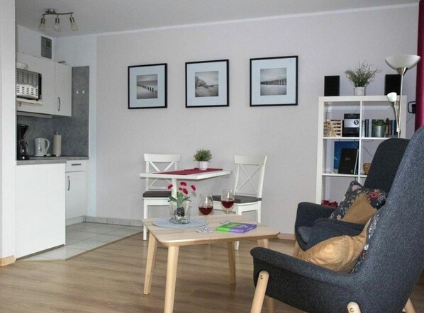 Ein Wohnzimmer mit Esstisch, zwei Stühlen, einer Couch und einem Bücherregal.