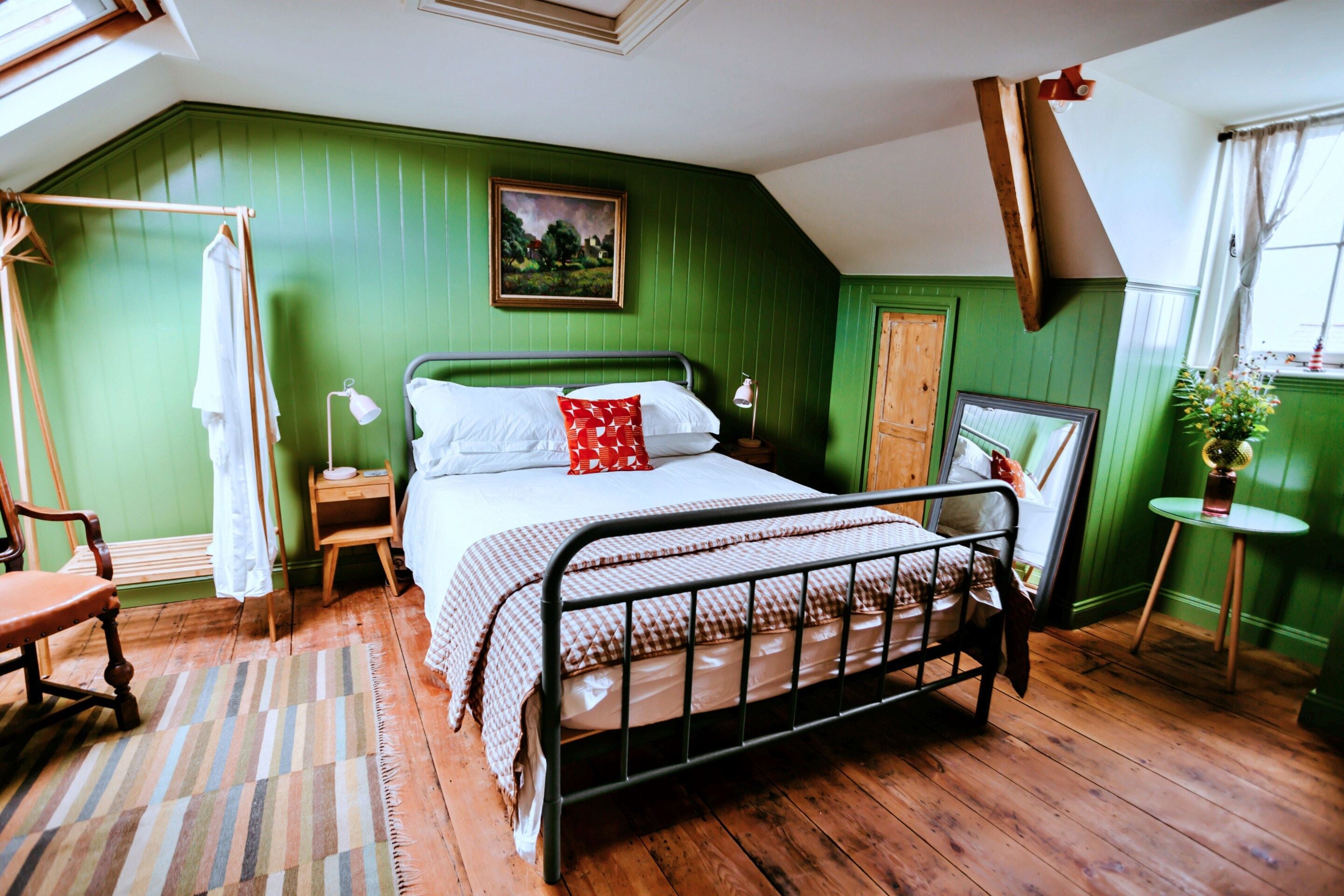 A bedroom with a bed, bedside tables, a chair, a window, and a painting on the wall.