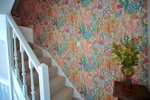 Eine Treppe mit weißer Handläufung und Teppichstufen führt zu einer Wand mit farbigem Blumenwallpaper.