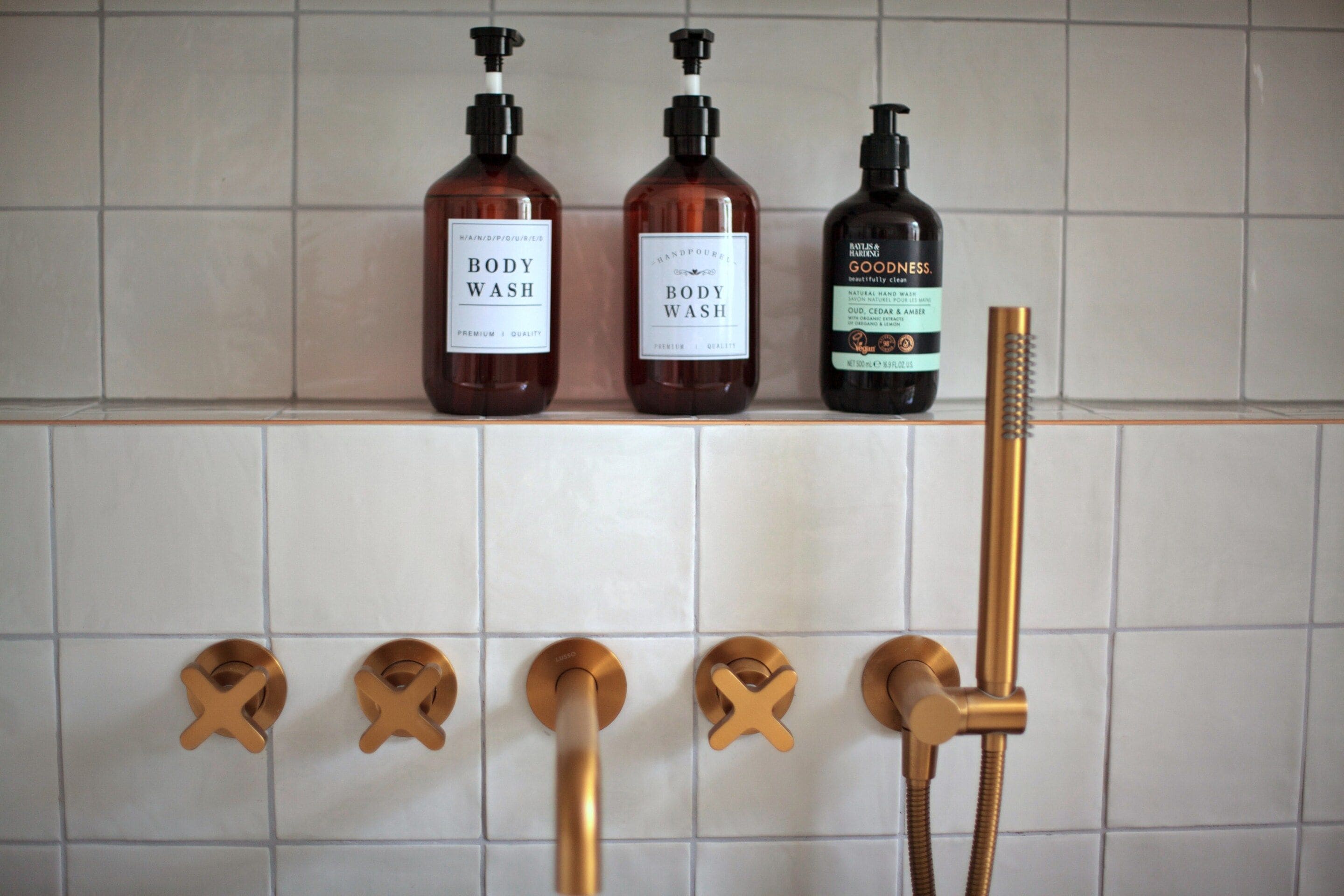 Three bottles of body wash on a shelf and a showerhead with a hose.