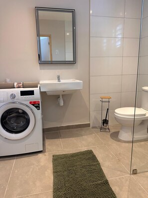 Un baño pequeño con lavadora, lavamanos, inodoro y espejo.