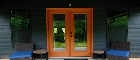 A double door entrance with glass panels, flanked by two wicker chairs with blue cushions, and a black doormat on the ground.