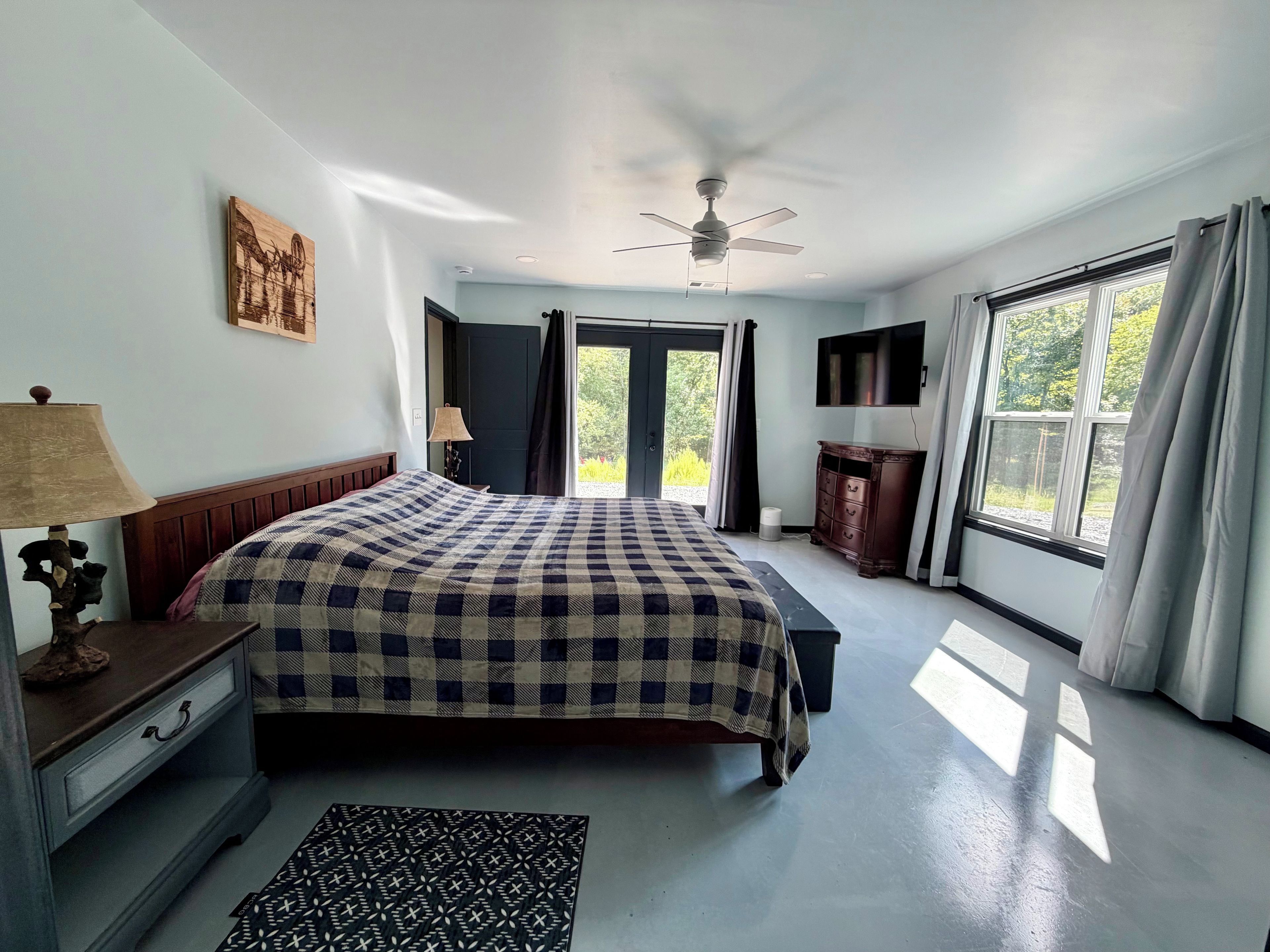 A bedroom with a bed, a ceiling fan, a dresser, a television, and a window with curtains.