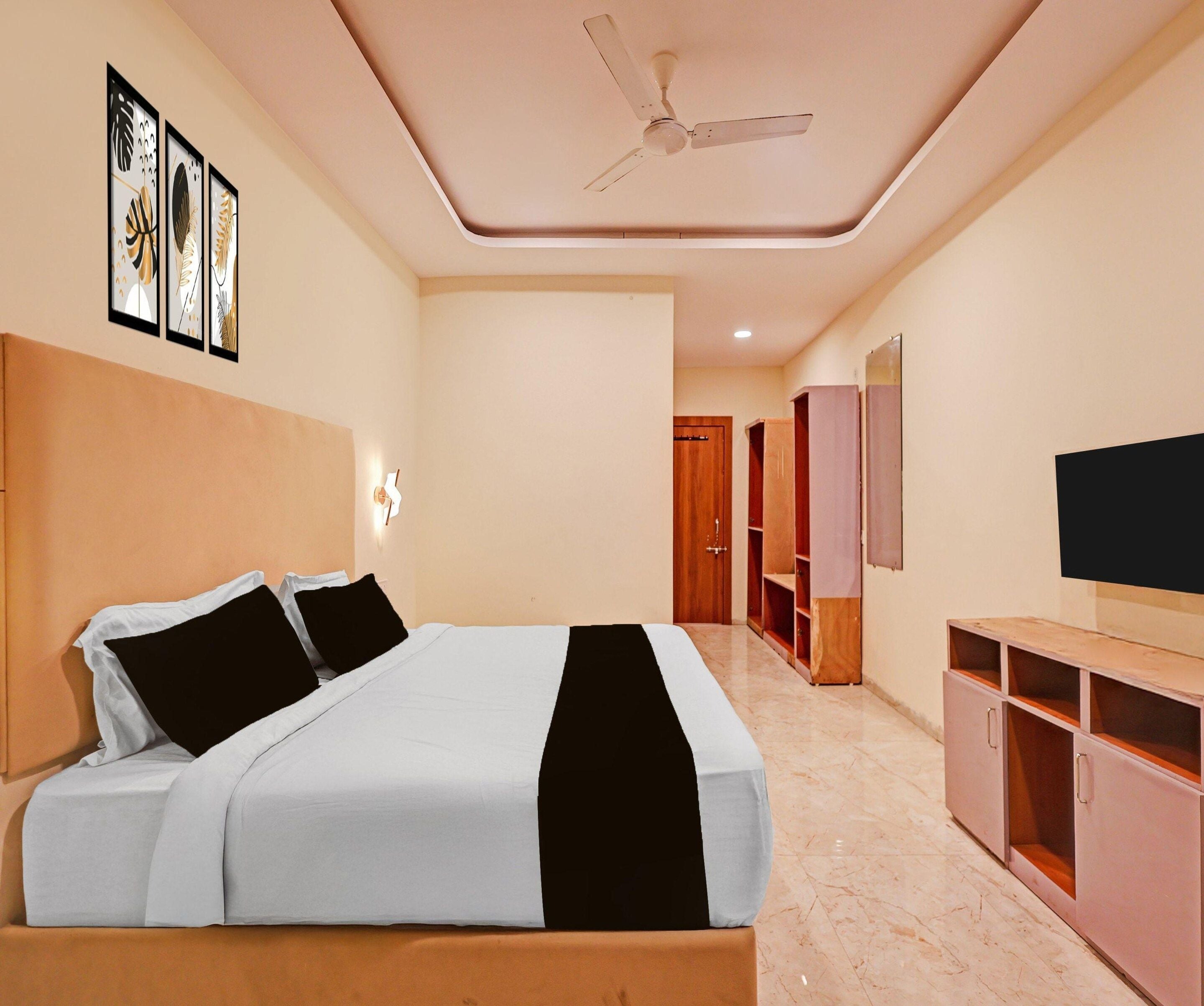 A hotel room with a bed, a ceiling fan, a TV, and a wardrobe.