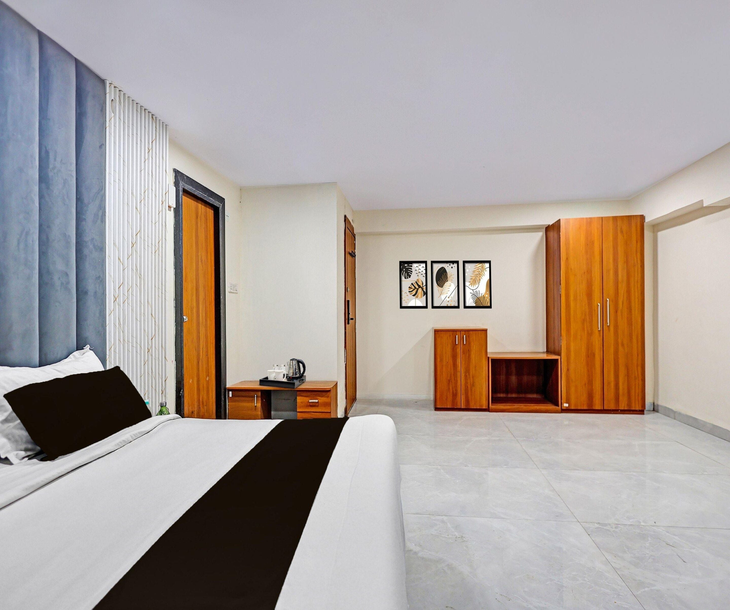 Een moderne slaapkamer met een bed, een houten garderobe, een bureau met waterkoker en een wand met ingelijste kunstwerken.