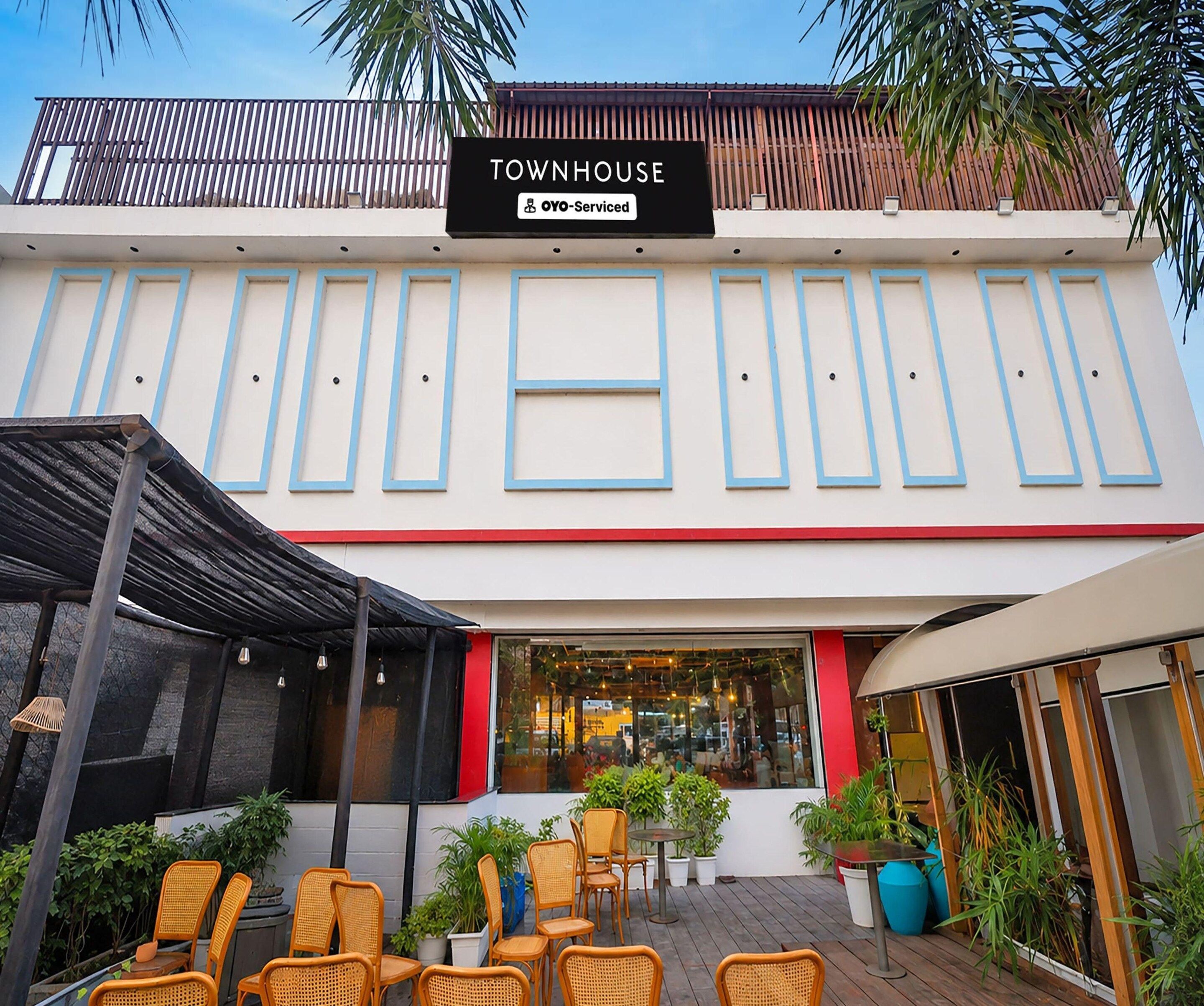 A building with a sign reading 'TOWNHOUSE' and 'OYO-Serviced'. There are outdoor seating areas with chairs and tables, and potted plants around.