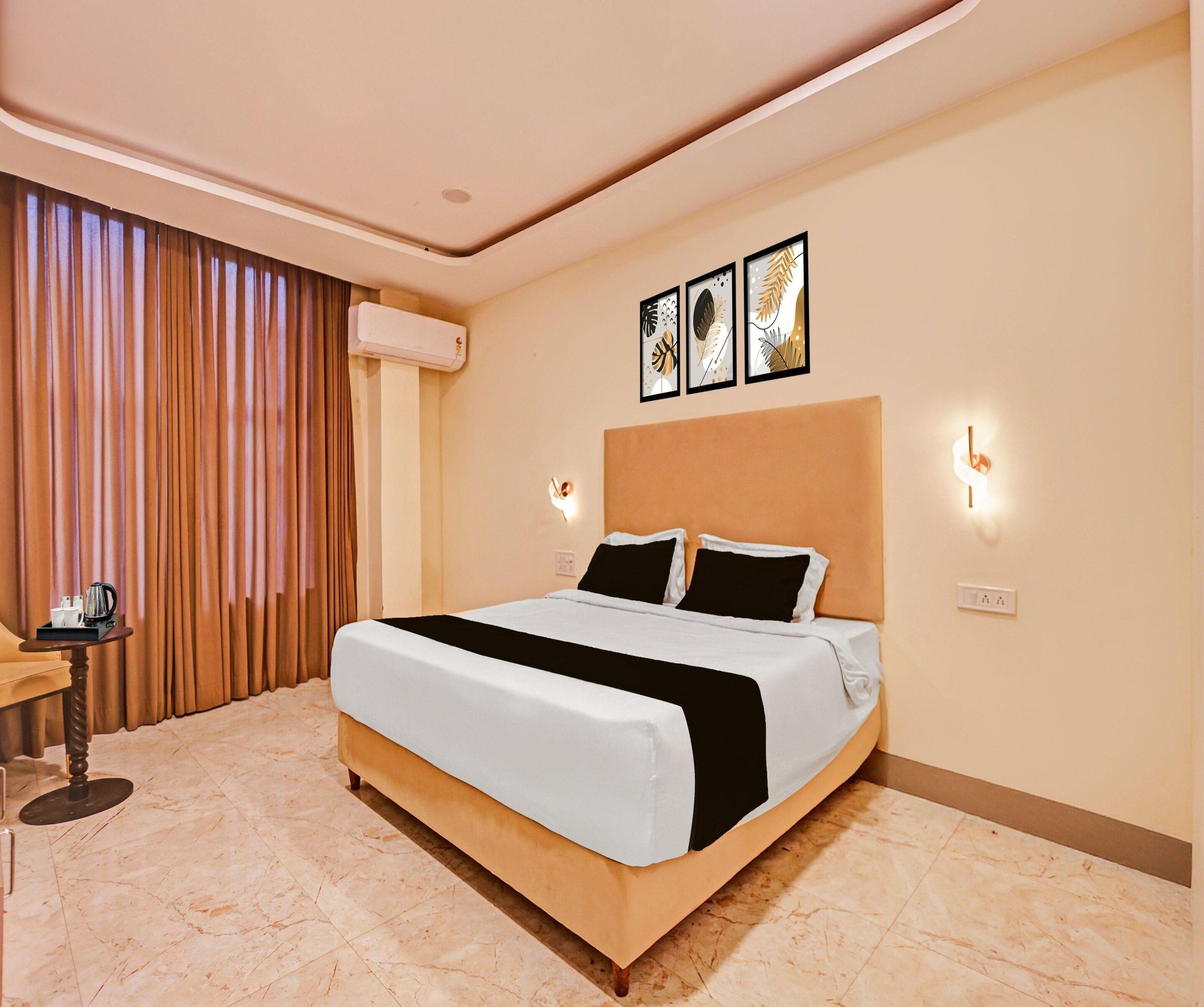 A hotel room with a bed, a bedside table with a coffee maker, and a wall-mounted air conditioner.