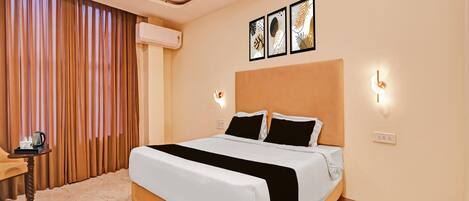 A hotel room with a bed, a bedside table with a coffee maker, and a wall-mounted air conditioner.