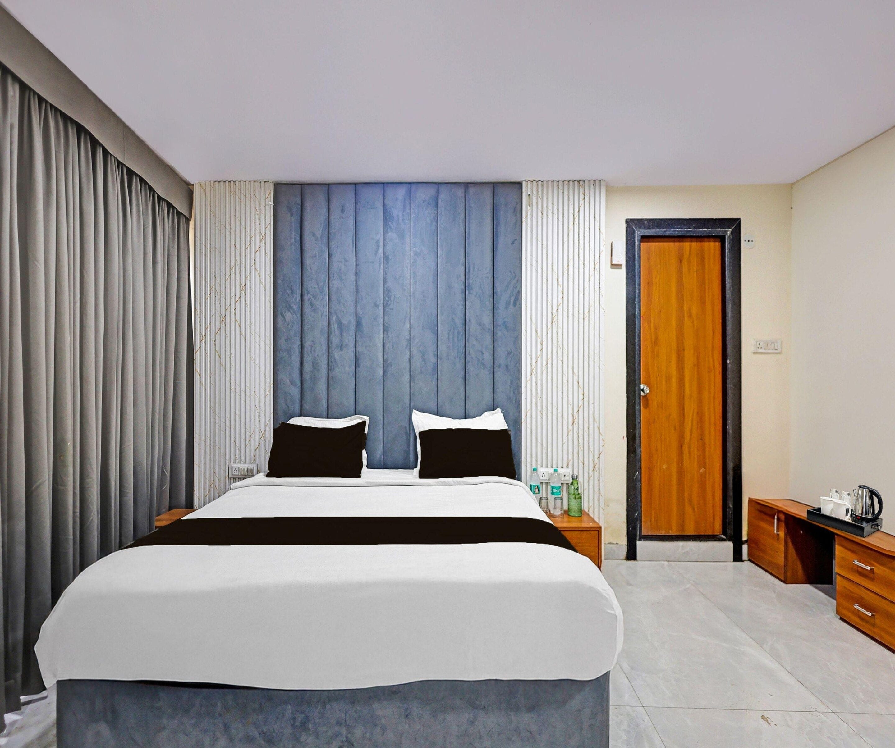 A hotel room with a large bed, a wooden wardrobe, a nightstand, and a door.