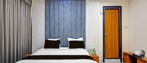 A hotel room with a large bed, a wooden wardrobe, a nightstand, and a door.
