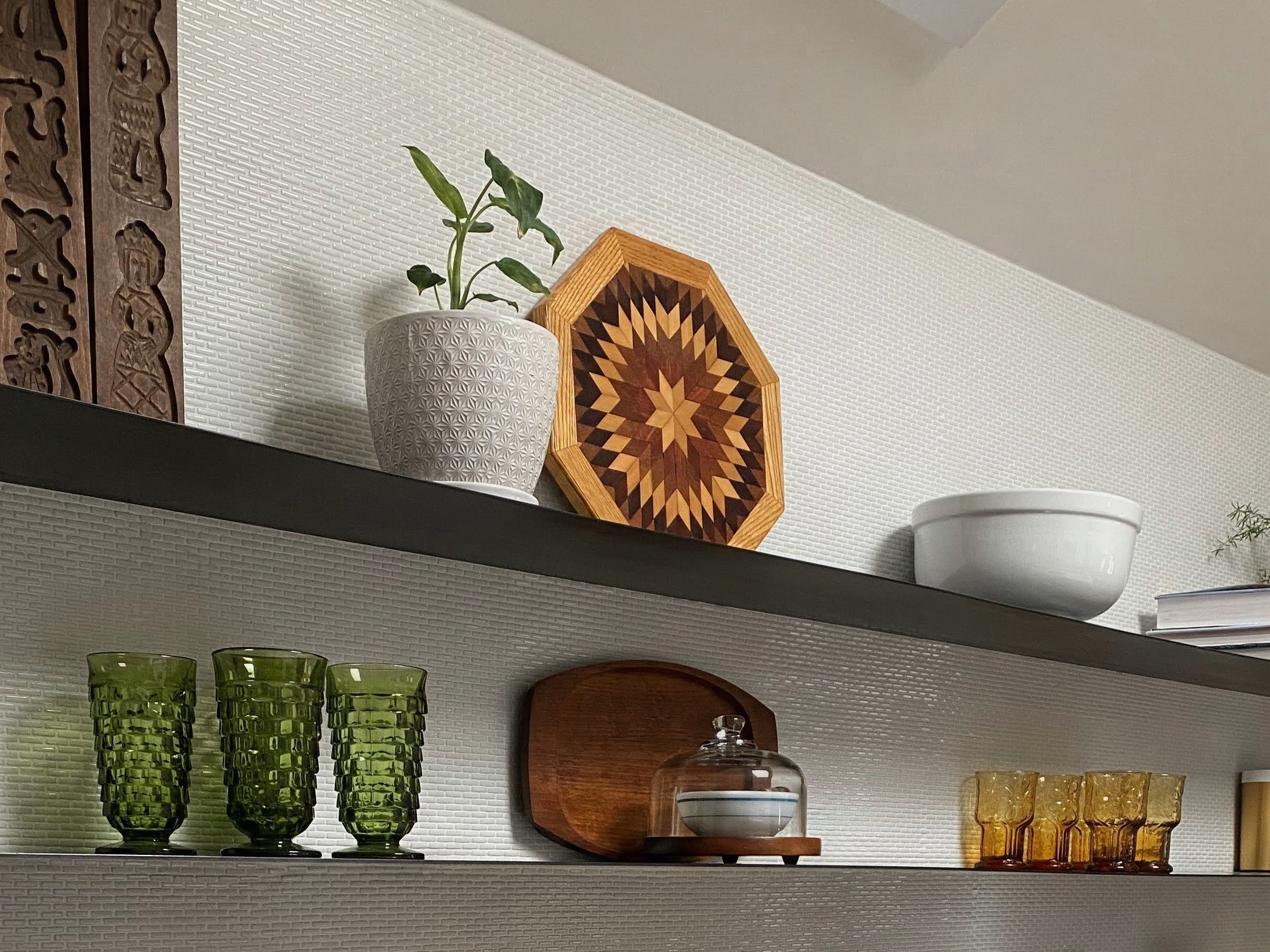 Une étagère ornée de divers objets décoratifs, notamment une plante, un objet en bois aux motifs géométriques et différents articles en verre.
