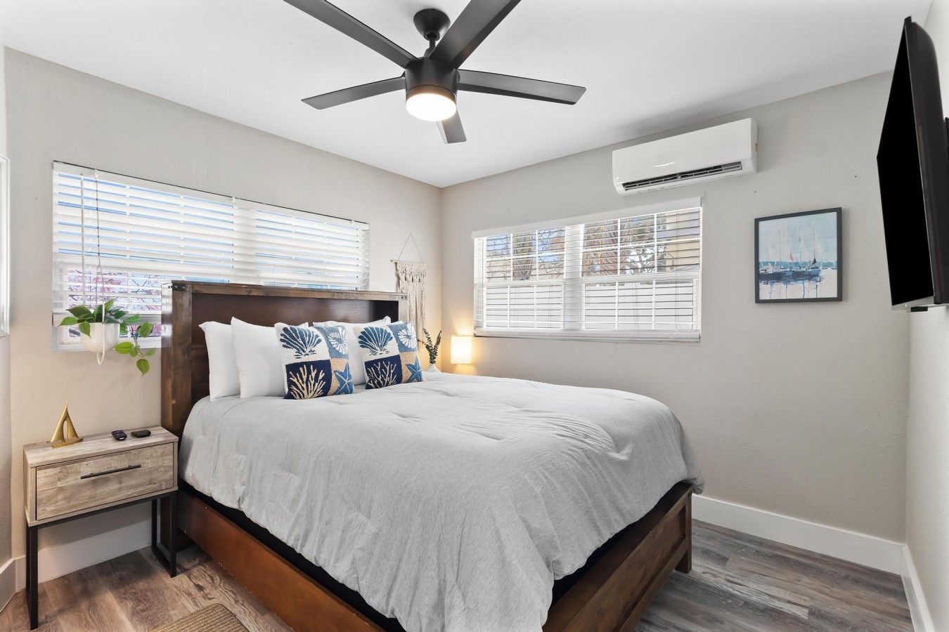 Une chambre à coucher avec un lit, des tables de chevet, un ventilateur de plafond et des fenêtres équipées de stores.