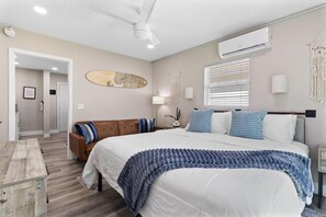 A bedroom with a bed, a brown sofa, a nightstand, a wall-mounted air conditioner, and a ceiling fan. - Sala Suite in St Pete Beach (St. Pete Beach)