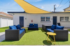 An outdoor seating area with wicker furniture and blue cushions, a yellow table, and a yellow shade sail. - Sala Suite in St Pete Beach (St. Pete Beach)