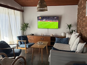 A living room with a television mounted on the wall, a wooden cabinet, a sofa, and a dining table.