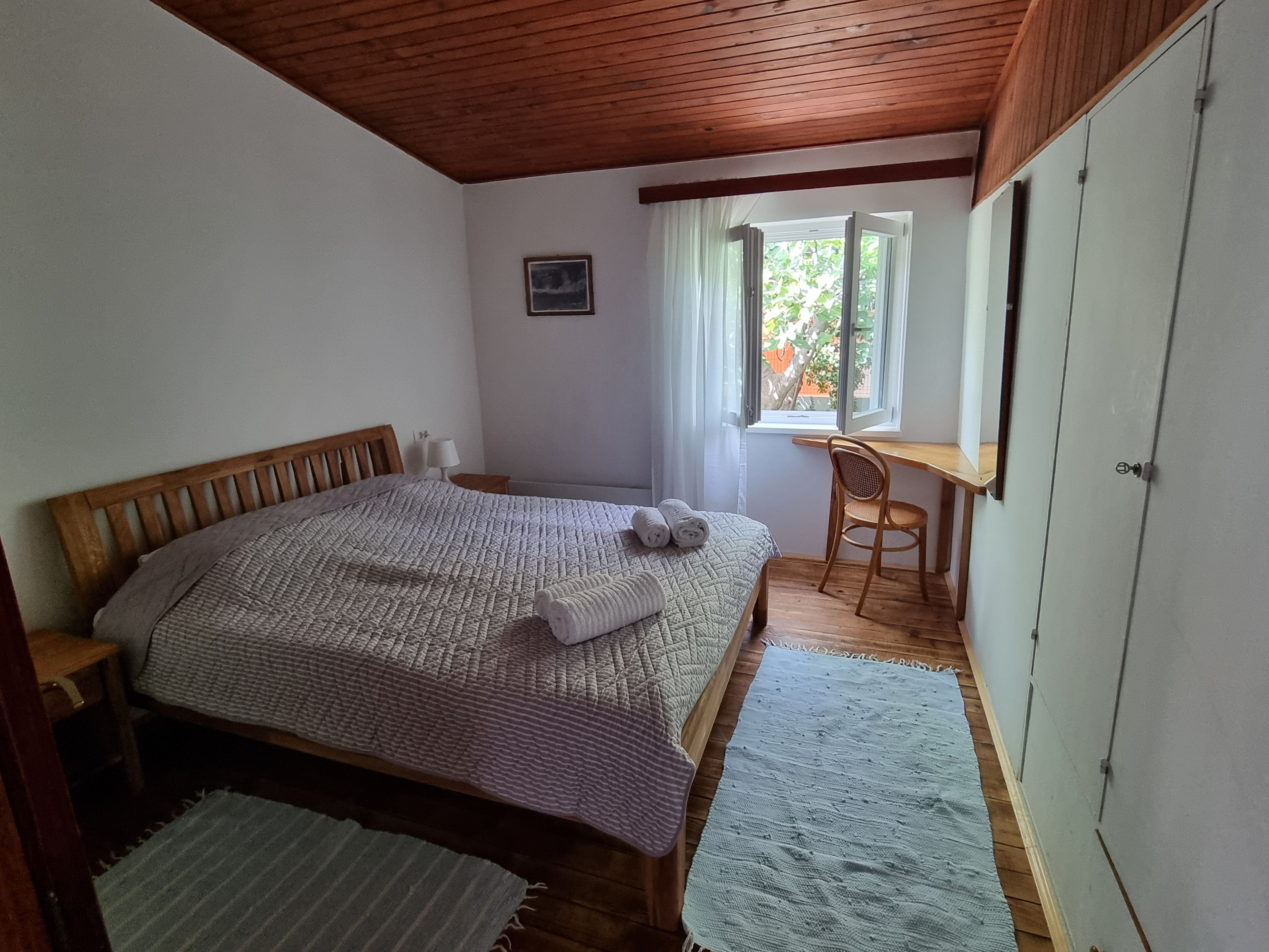 A bedroom with a wooden bed, a desk, and a window.