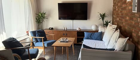 Una sala de estar con televisor de pantalla plana, un sofá, una mesa de centro y dos sillones.