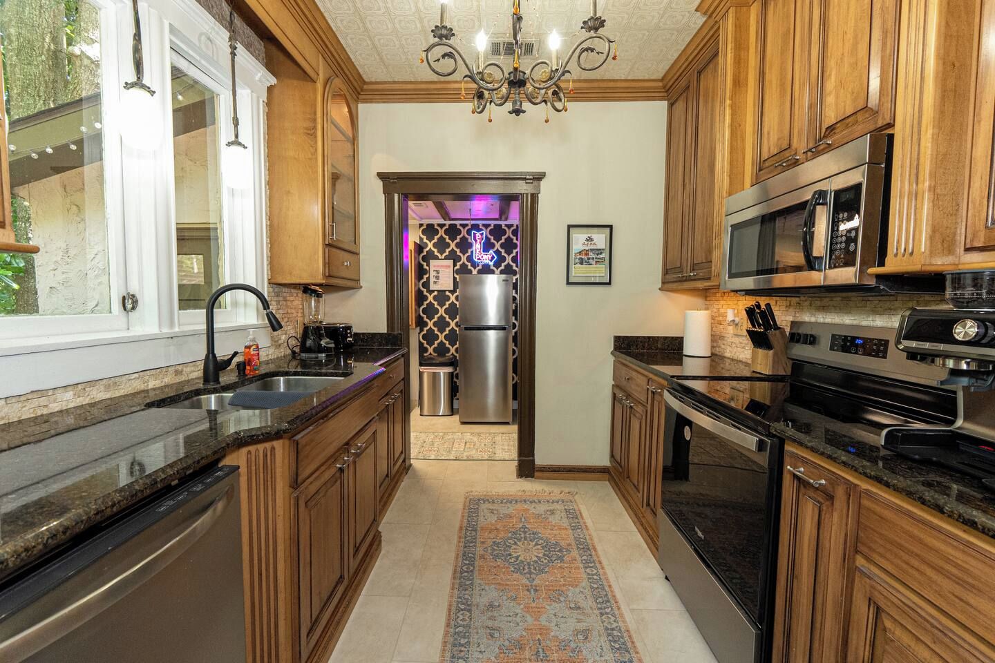 A kitchen with wooden cabinets, stainless steel appliances, a chandelier, and a patterned rug.