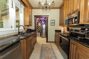 A kitchen with wooden cabinets, stainless steel appliances, a chandelier, and a patterned rug. - Historic Gulf Hills Speakeasy with Hot Tub - 3 Min to Downtown OS (Ocean Springs)