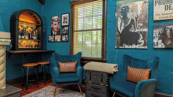 A room with teal walls, two blue armchairs with brown cushions, a bar area with bottles and glasses, and a window with blinds.