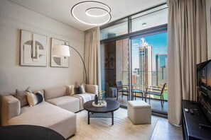 A modern hotel room with a sofa set, a coffee table, a TV, and a balcony with a city view. - New Waterfront 1B with Skyline & Canal View (Dubai)