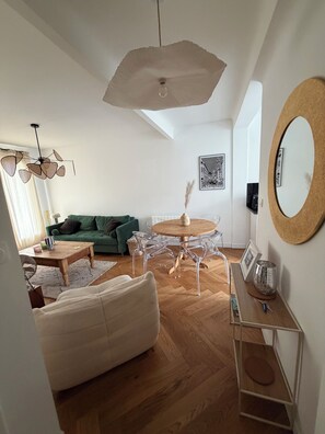 A modern living room with a green sofa, a round wooden table with chairs, a hanging light fixture, and a large mirror on the wall. - Tremendous 1-bedroom apartment in cool Le Havre near the beach (Le Havre)