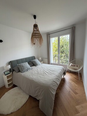 A bedroom with a bed, bedside tables, a hanging light fixture, a chair, and a window with a view of greenery. - Tremendous 1-bedroom apartment in cool Le Havre near the beach (Le Havre)