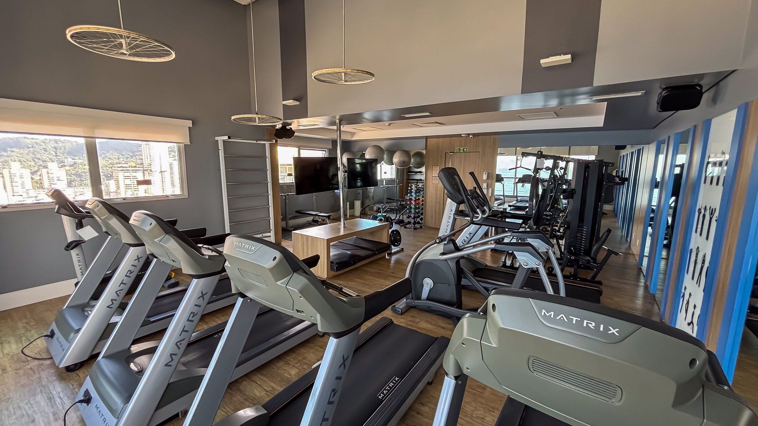 A gym with treadmills, weight machines, and a large window with a city view.