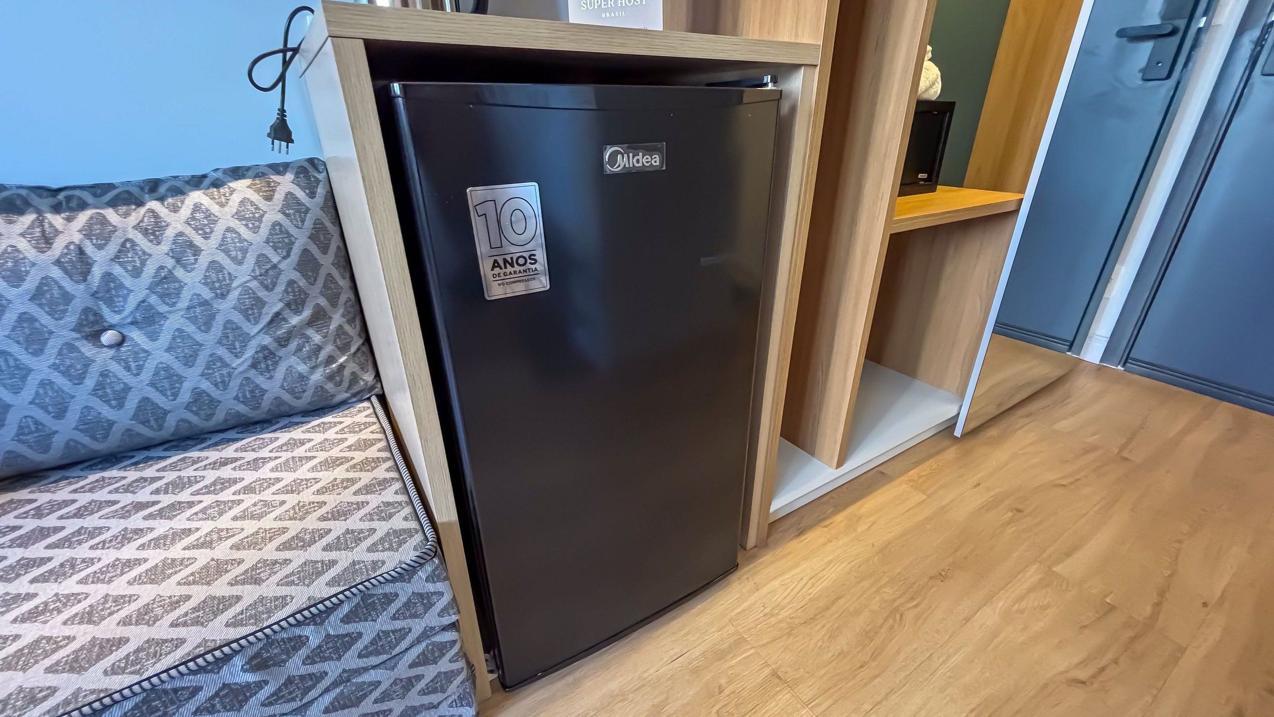 Un refrigerador negro compacto en una kitchenette con un sofá estampado y piso de madera.