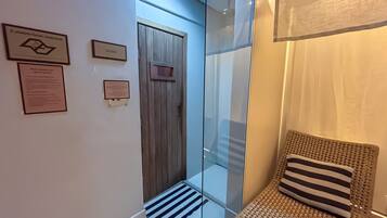 Un área de spa con una puerta de madera, un panel de vidrio y una silla de mimbre con un cojín a rayas.