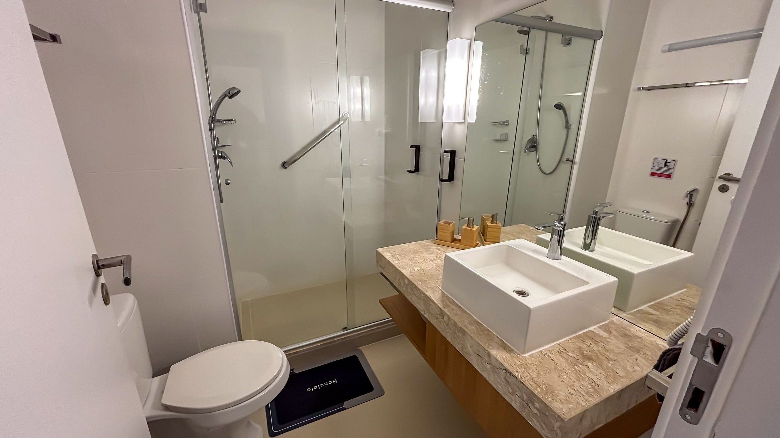 Um banheiro moderno com box de vidro, vaso sanitário, pia e um espelho grande.