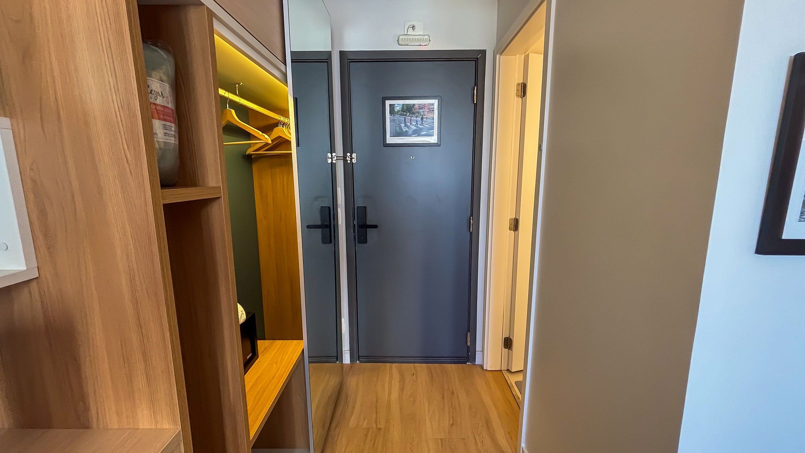 Um corredor com uma prateleira de madeira, um cabideiro e uma porta cinza com um quadro.